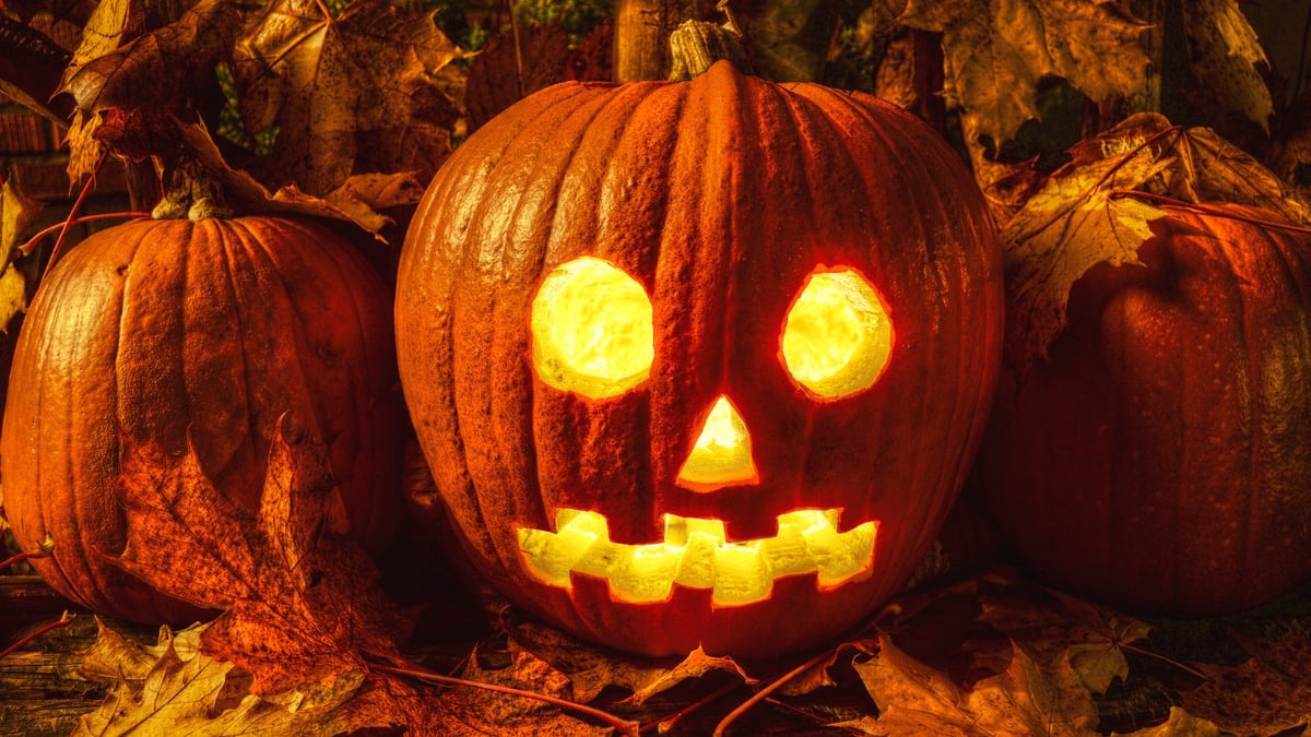 A glowing jack-o'-lantern surrounded by autumn leaves, perfect for Halloween themes.